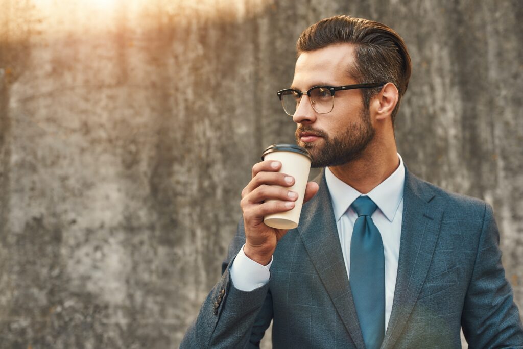 Confident and successful. Young businessman in formal wear and eyeglasses drinking coffee and